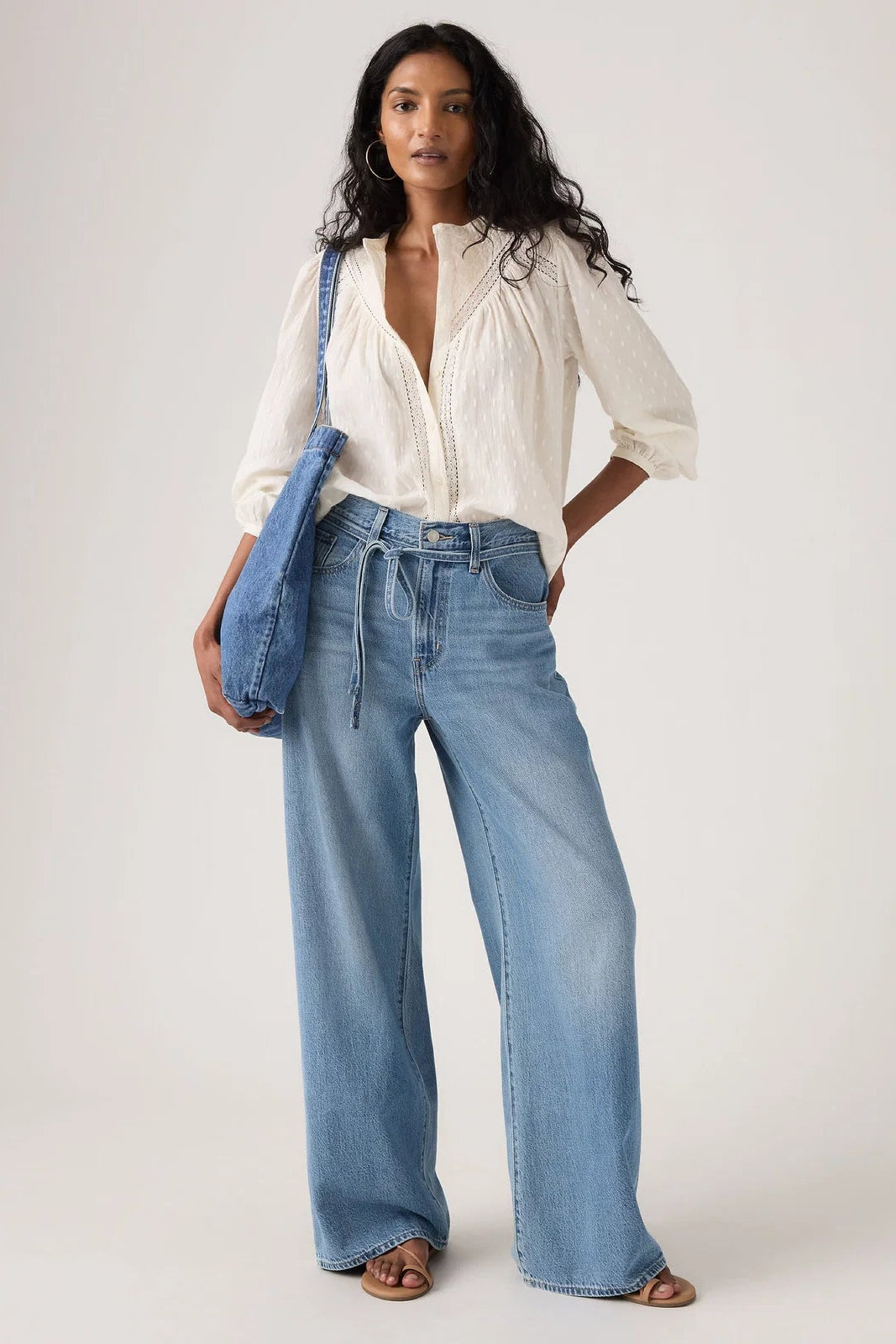 Woman wearing a white blouse and blue jeans with a blue bag on a white background